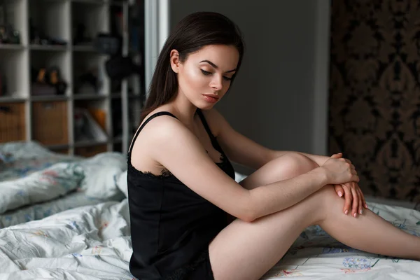 Vacker kvinna i svarta underkläder sitter på en säng — Stockfoto