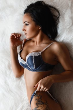 Şık dövme kürk üzerinde yatan şık genç esmer şehvetli kadın, yan bakıyor.