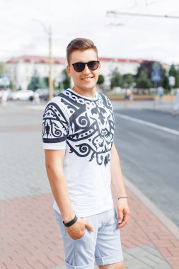 Güneş gözlüğü, T-shirt ve şort şehrin arka plan üzerinde şık genç adam.