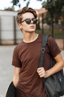 Güneş gözlüğü şık yakışıklı adam ve bir yaz gününde bir kaykay tutan bir çanta.