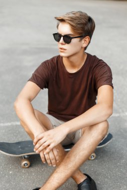 Genç yakışıklı bir saç modeli ve kaykay üzerinde dinlenme güneş gözlüğü.