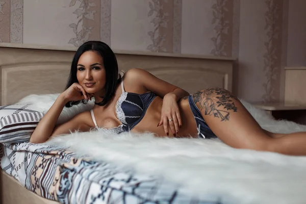 Vacker flicka med en tatuering i underkläder på kroppen som ligger på sängen — Stockfoto
