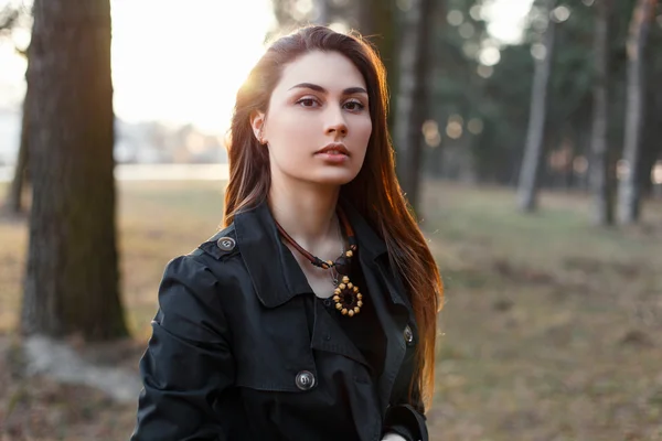 Junges stilvolles Mädchen in schwarzem Mantel im Park bei Sonnenuntergang. — Stockfoto