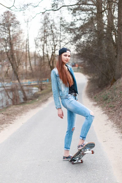 年轻漂亮的女孩，与滑板站在沥青道路上. — 图库照片