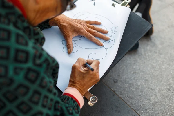 A idosa de óculos está desenhando sobre papel. Mão segurando uma caneta — Fotografia de Stock