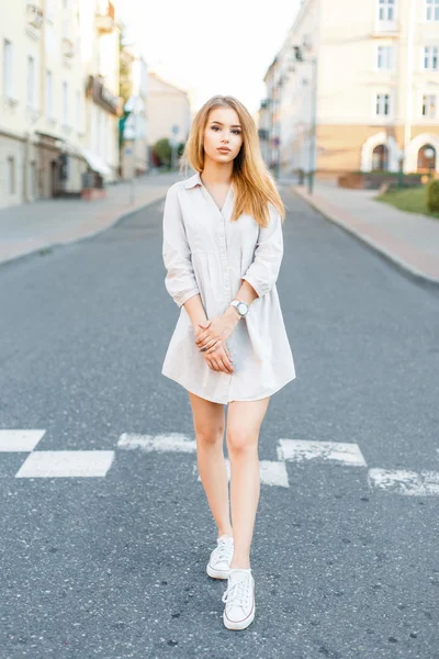 Jeune belle fille avec des vêtements à la mode marchant sur la route sur le fond de la ville . — Photo