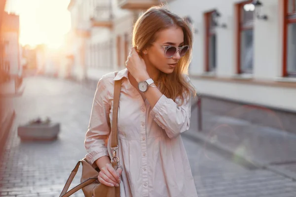 Giovane bella ragazza in occhiali da sole alla moda e con una borsa alla moda al tramonto . — Foto Stock