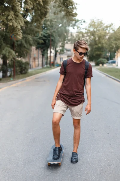 Jeune beau mec en lunettes de soleil chevauchant sur un skateboard . — Photo