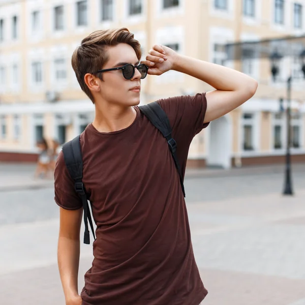 Молодий стильний чоловік виправляє сучасні сонцезахисні окуляри на тлі міста — стокове фото