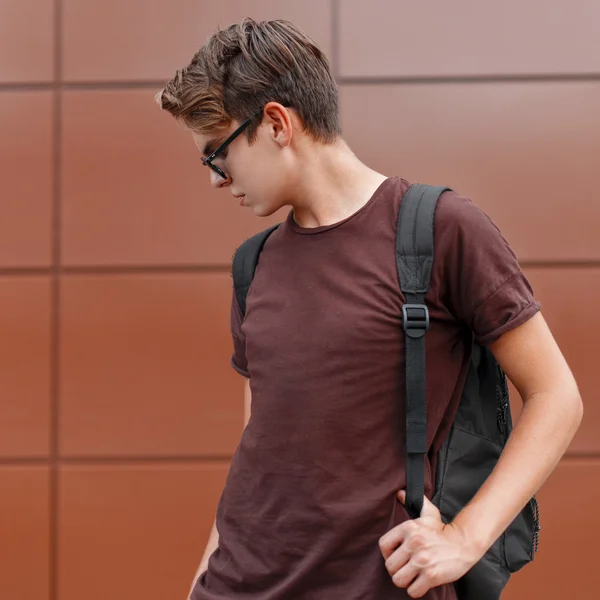 Homem bonito jovem em uma camiseta e óculos de sol, segurando uma mochila . — Fotografia de Stock