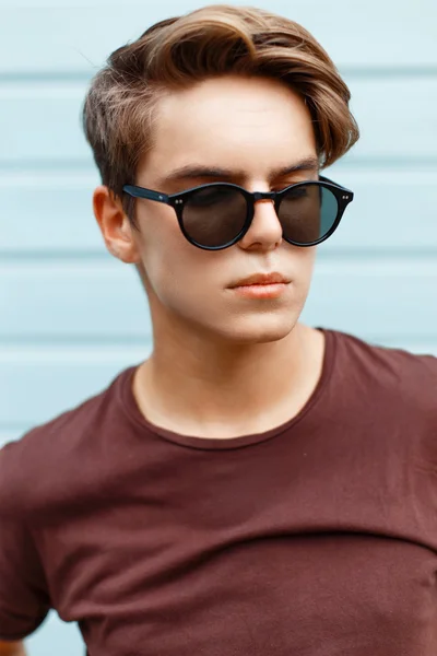 Retrato de primer plano de un hombre guapo con el peinado en gafas de sol sobre un fondo azul brillante . — Foto de Stock