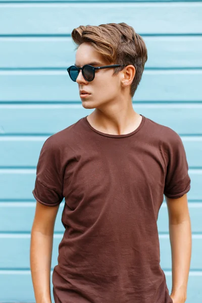 Hombre guapo en gafas de sol de pie cerca de la pared de madera azul . — Foto de Stock