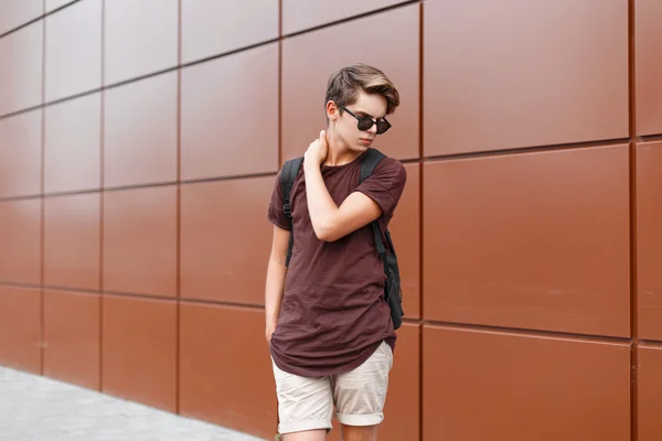Красива стильна людина з сонцезахисними окулярами і рюкзаком, що стоїть біля металевої стіни . — стокове фото