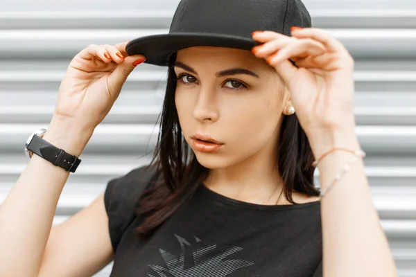 Güzel genç kız siyah beyzbol şapkası ve t-shirt ayakta duvarın yanında — Stok fotoğraf