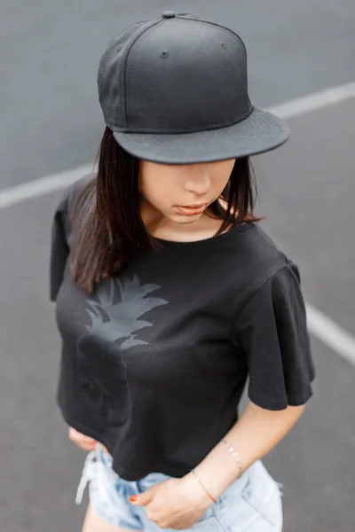 Schönes Mädchen im Swag-Stil schwarzes T-Shirt und eine Mütze im Stadion. — Stockfoto