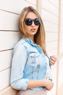 Güneşli bir günde ahşap bir duvarın yanında duran güneş gözlüğü ve kot ceket pretty kadın