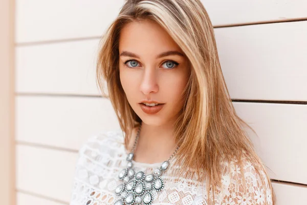 Portrait d'une belle jeune fille en robe élégante avec des bijoux sur une plage, se tient près d'un mur en bois léger . — Photo