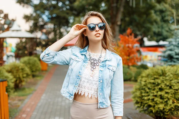 Menina bonita em óculos de sol e jaqueta jeans andando nas atrações do parque — Fotografia de Stock