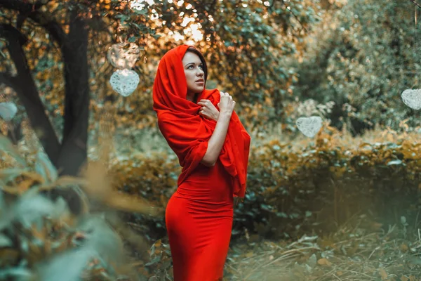 Hermosa chica en un vestido rojo de pie en el jardín con corazones — Foto de Stock