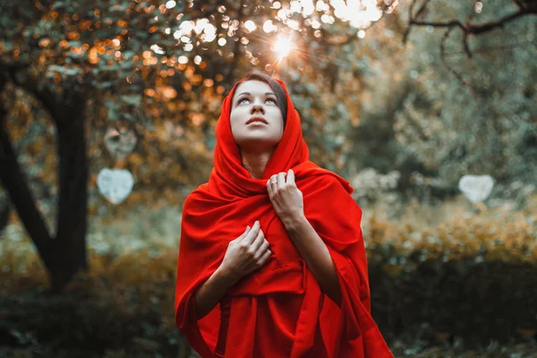 Chica en un vestido rojo de pie mirar hacia arriba en el jardín con corazones — Foto de Stock