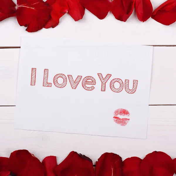 张纸的文字我爱你用一个吻。请注意，将玫瑰花瓣撒在桌子上 — 图库照片