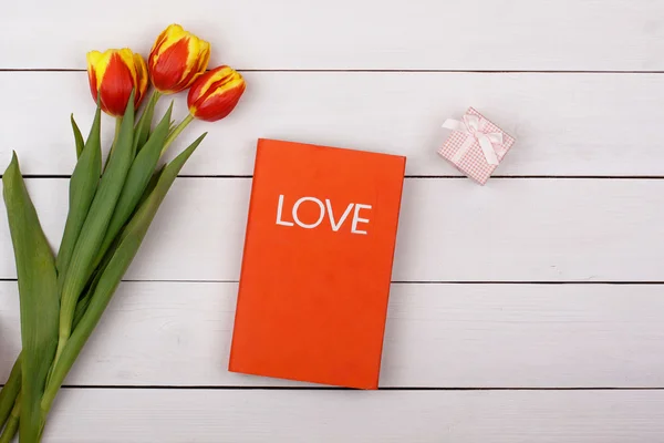 빨간 책 사랑 흰색 테이블에 놓여 있습니다. 튤립 꽃과 선물 — 스톡 사진