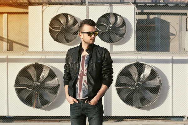 Retrato de un hombre hipster en una chaqueta de cuero negro y gafas de sol — Foto de Stock