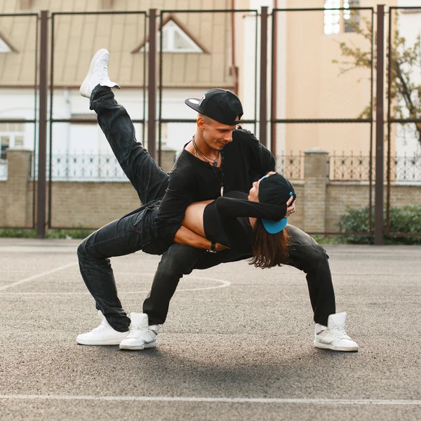 Hermosa pareja joven bailando hip-hop en el estadio. El tipo sosteniendo a la chica en sus brazos . — Foto de Stock