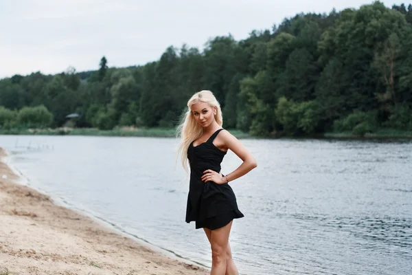 Hermosa chica en vestido negro en la orilla del río — Foto de Stock