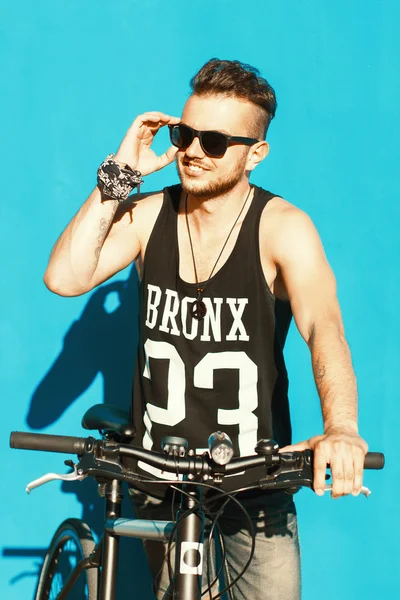 Hipster met een fiets in de buurt van een heldere blauwe muur. — Stockfoto