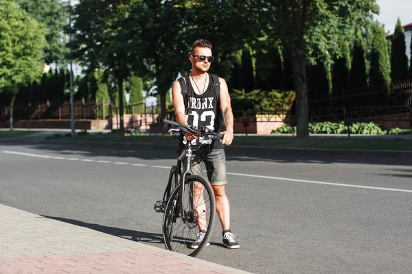 Jovem homem elegante de pé na estrada com a moto — Fotografia de Stock