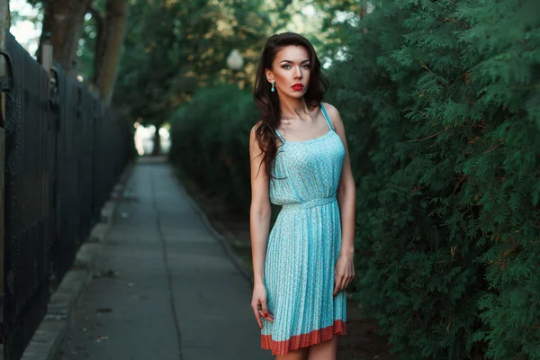 Mujer bonita en un vestido con pendientes cerca del arbusto verde . — Foto de Stock