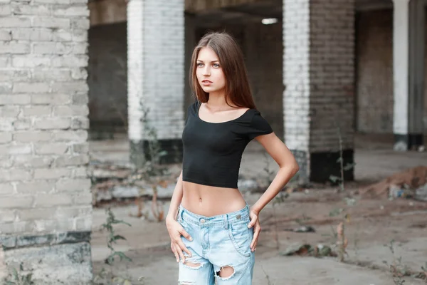 Beautiful girl in a black T-shirt and torn jeans near the brick columns.