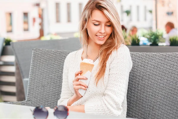 Красивая девушка сидит в летнем кафе и ест мороженое в вафельном конусе. Женщина держит в руках вафли с мороженым . — стоковое фото