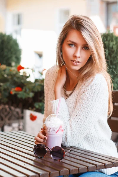 Ładna kobieta w białym swetrze siedzi w letniej kawiarni i picia koktajl — Zdjęcie stockowe