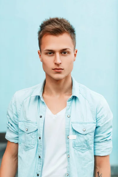 Gros plan portrait d'un jeune homme élégant dans une chemise en denim près d'un mur bleu . — Photo