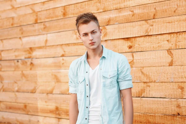 Joven hombre guapo en un vestido de mezclilla cerca de la pared de madera — Foto de Stock