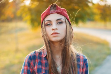 Autumn portrait of a beautiful girl in a baseball cap and a shirt at sunset.