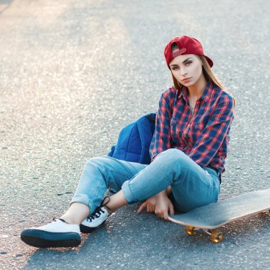 Beautiful young girl sitting on the asphalt with a skateboard. Outdoor lifestyle picture on a sunny summer day