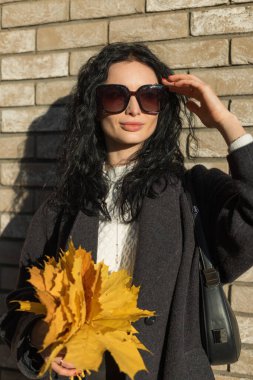 Koyu kıvırcık saçlı, açık havada renkli yapraklar tutan, sıcak sonbahar tonları ve doğal ışıkla çevrili çekici bir kadın manken..