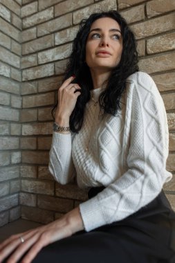 Sonbahar kıyafetleri içinde, dışarıda güneşin altında oturmuş huzurlu bir öğleden sonranın sıcaklığının tadını çıkaran zarif genç bir bayan model..