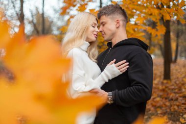 Altın yapraklarla çevrili bir sonbahar parkında kucaklaşan romantik çift. Sıcak sonbahar renkleri, açık havada sevgi ve şefkat..