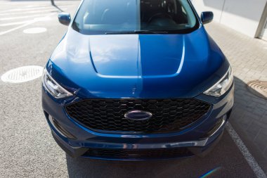 Şehir ortamında mavi modern SUV, yakın çekim farı ve kalın ön tasarım.