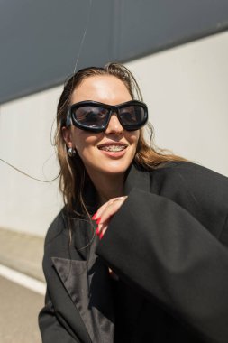 Büyük boy spor ceket ve güneş gözlüklü şık bir model, neşeli bir hareketle poz veriyor, yaşam tarzı, sokak kıyafetleri ve moda kavramları için mükemmel..