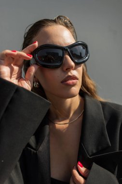 Şık giyimli şık şehir kadını şehirde güneş ışınlarında havalı güneş gözlüğü takıyor. Sokaktaki güzel kız..