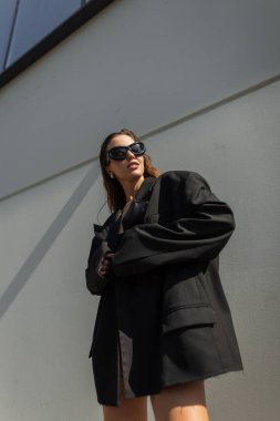 Kendine güvenen, modaya uygun sokak kıyafetleri giyen, güneş gözlüğü takan ve büyük beden ceket giyen bir kadın. Modern şehir moda fotoğrafçılığı.