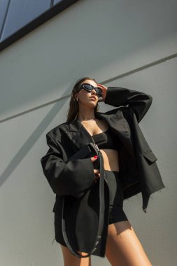 Şık bir kız, büyük bir spor ceket ve siyah bir bluz giyiyor. Açık havada cesur bir tavırla poz veriyor. Modern moda ve yaşam tarzı sahnesi.