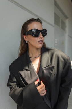 Zarif siyah ceketli ve güneş ışığında poz veren modaya uygun siyah güneş gözlüklü, çağdaş şehir tarzı konsept..