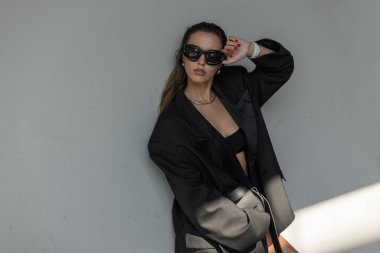 Kalın sokak kıyafetleri içinde moda bir kadın, büyük beden ceket ve güneş gözlüğü, modern şehir atmosferiyle dışarıda poz veriyor..