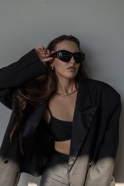 Kendine güvenen bir kadının modern moda portresi. Büyük beden ceketli ve güneş gözlüklü, modaya uygun şık şehir tarzında poz veriyor..